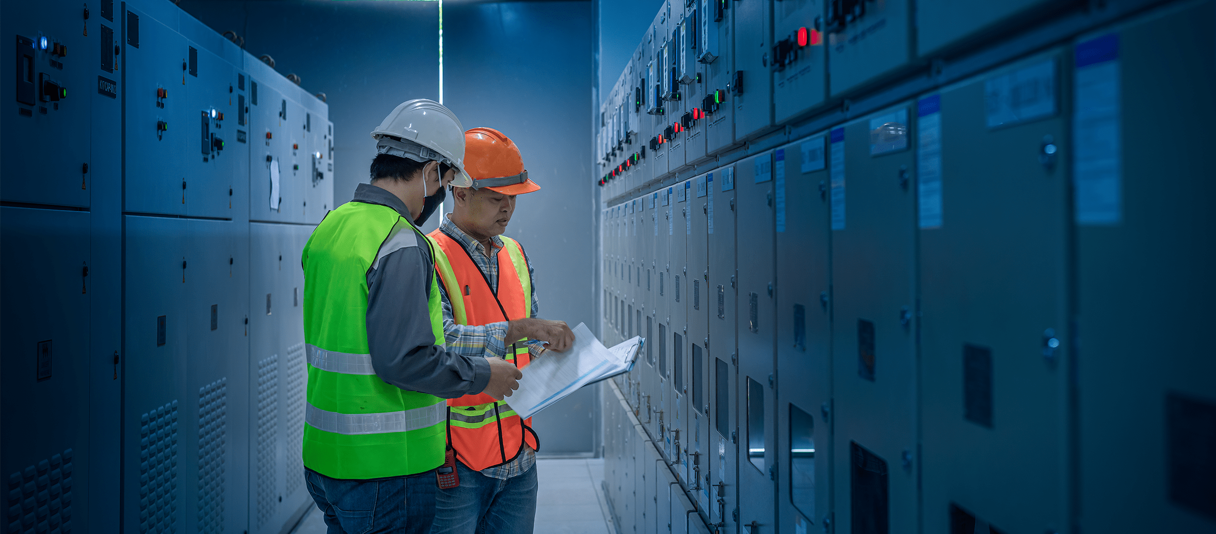Photograph of two electrical workers in PPE reviewing paperwork near an electrical system