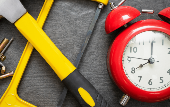 Red alarm clock sitting next to a crossed hammer and saw, with screws.