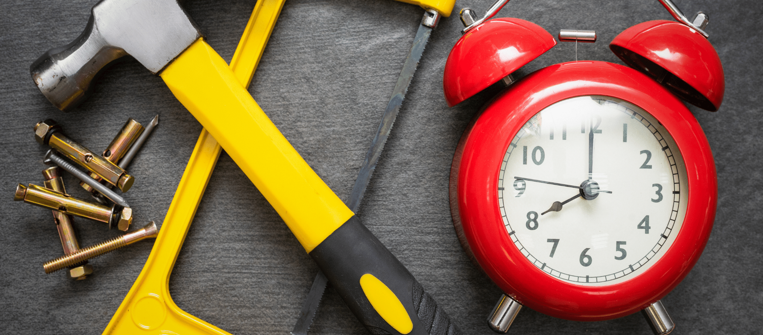 Red alarm clock sitting next to a crossed hammer and saw, with screws.